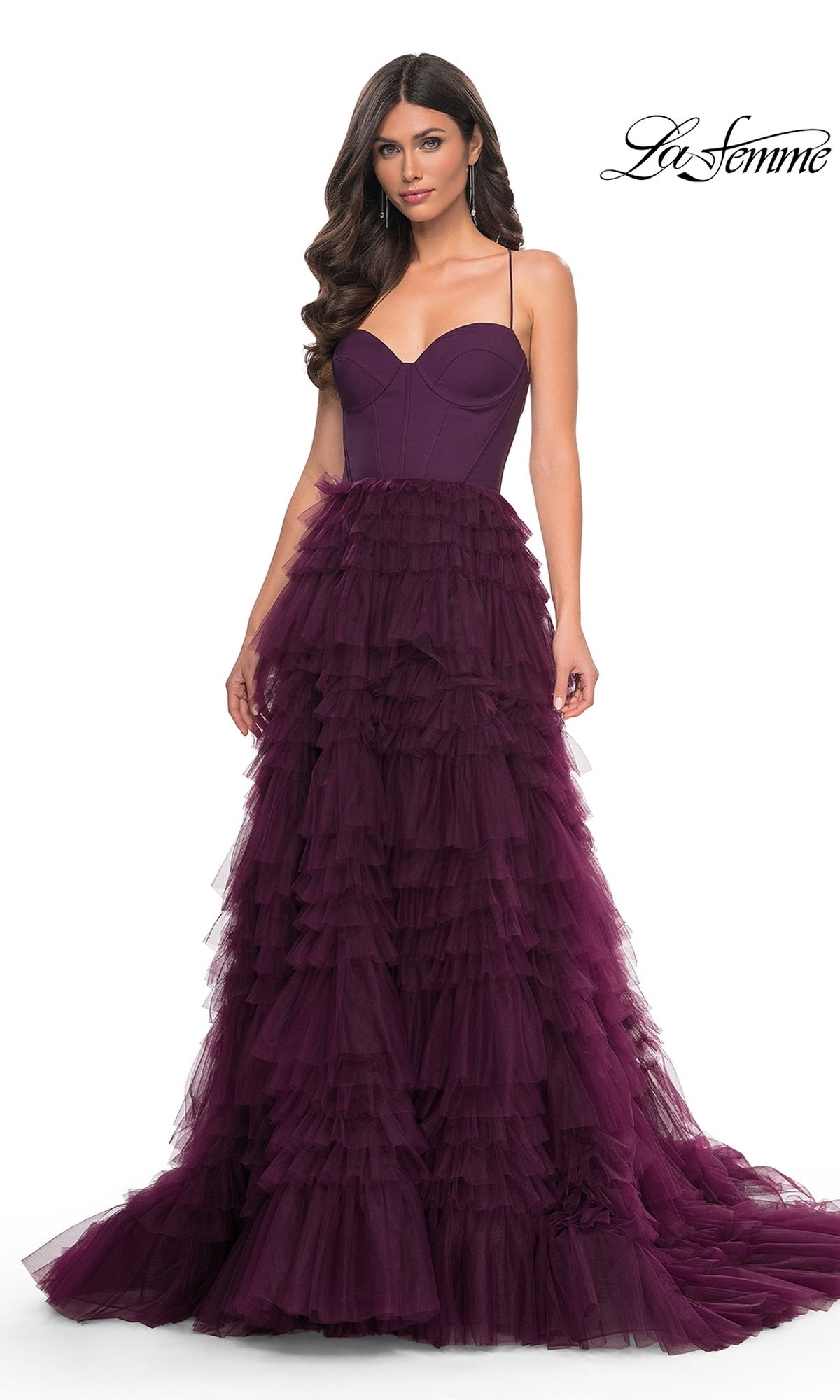 A woman wears the La Femme 32071 Lace-Up Ruffle Long Prom Ball Gown, featuring a sleeveless sweetheart corset bodice and spaghetti straps, as she stands against a white background.